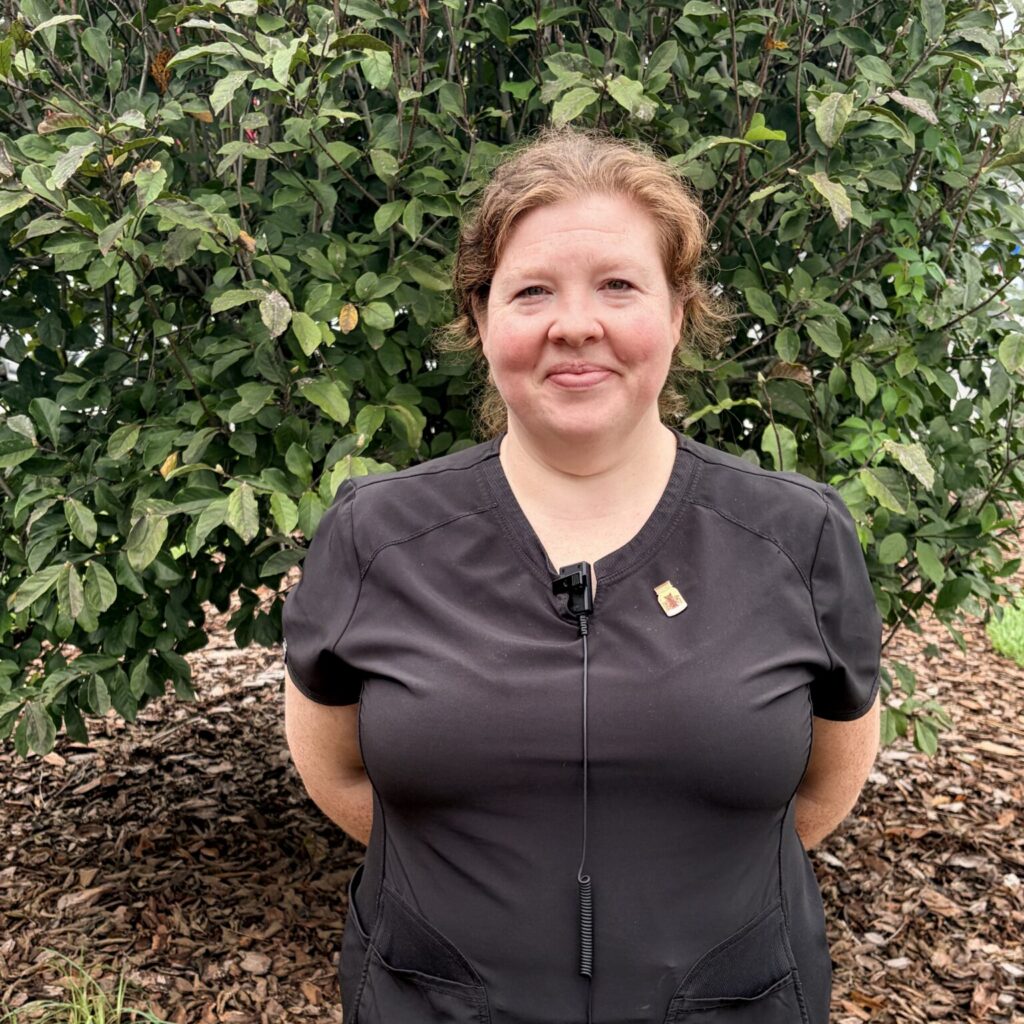Ashley smiling and standing outside in front of a tree